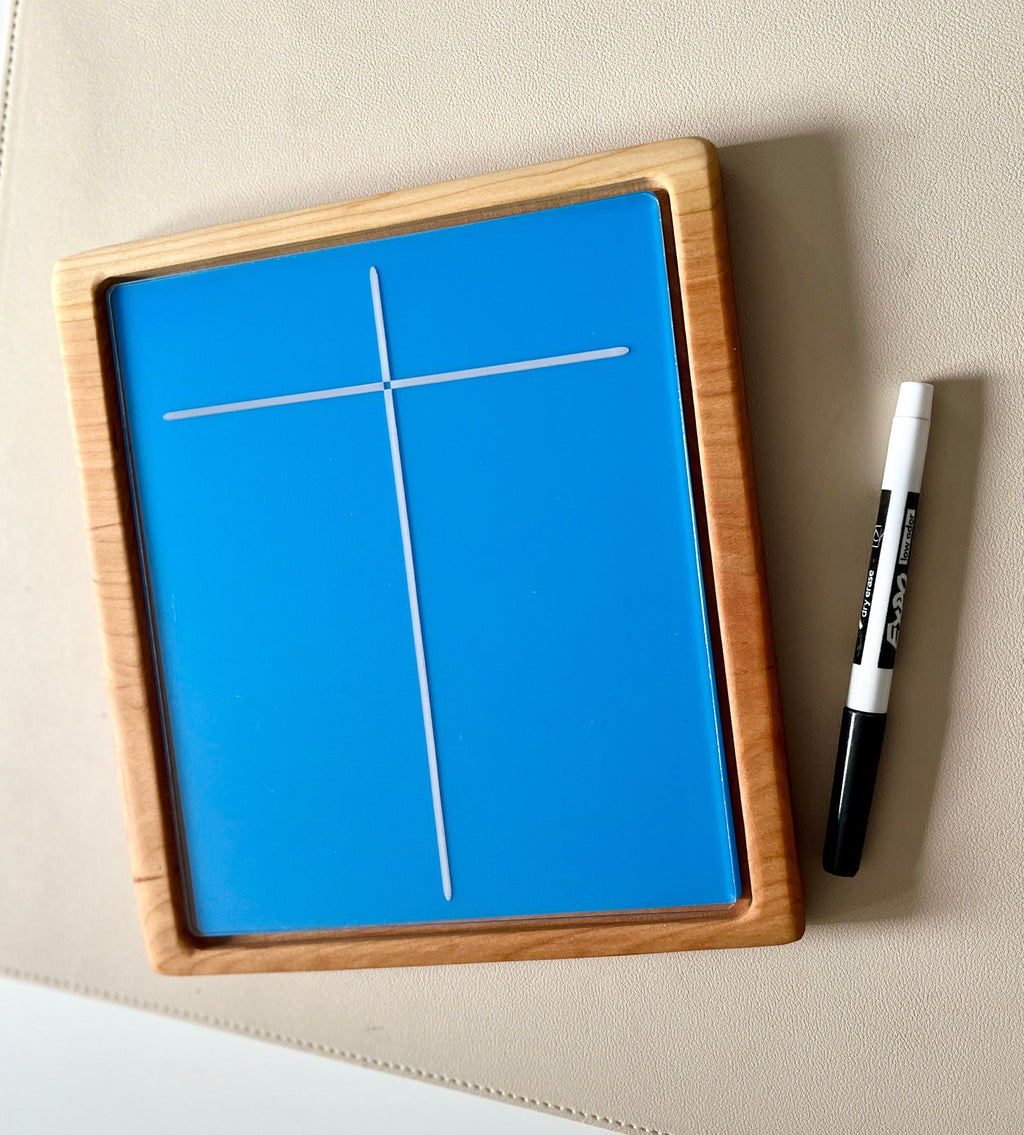 Rectangular wooden frame with blue dry erase board showing a white cross and a black dry erase marker on beige surface