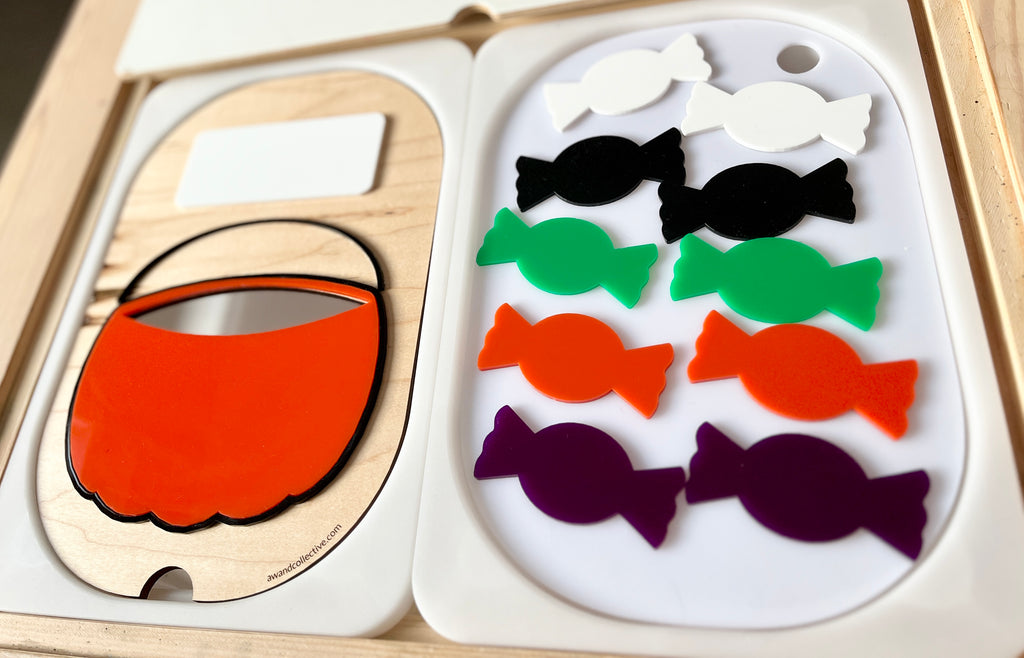 Set of colorful candy-shaped pieces in black, white, green, orange, and purple with an orange basket cutout on wooden and white trays