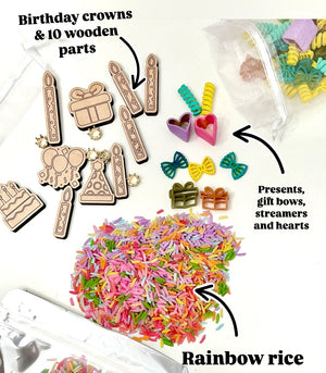 Assorted wooden birthday shapes, colorful gift bows, hearts, streamers, and multicolored rainbow rice on white surface