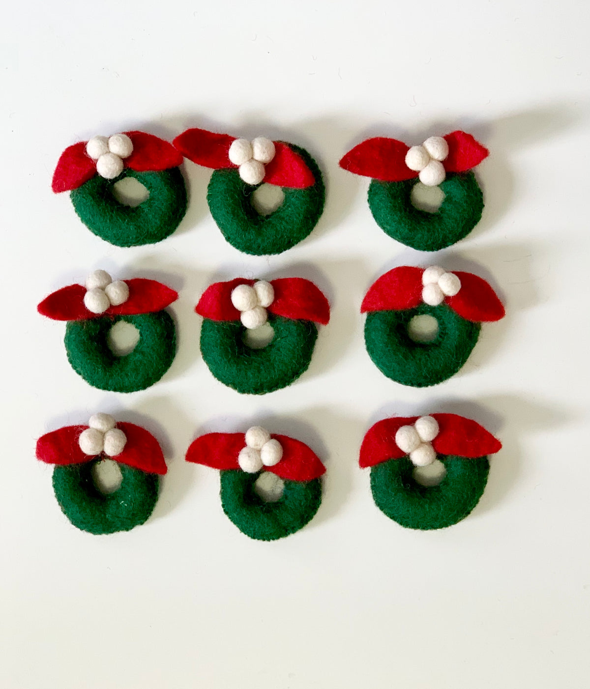 Set of handmade green felt wreaths with red leaves and white berries on white background arranged in rows