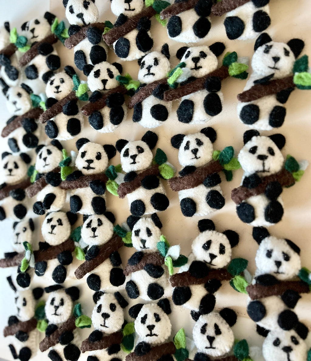 Numerous small felt panda figures holding brown branches with green leaves arranged closely on a light surface