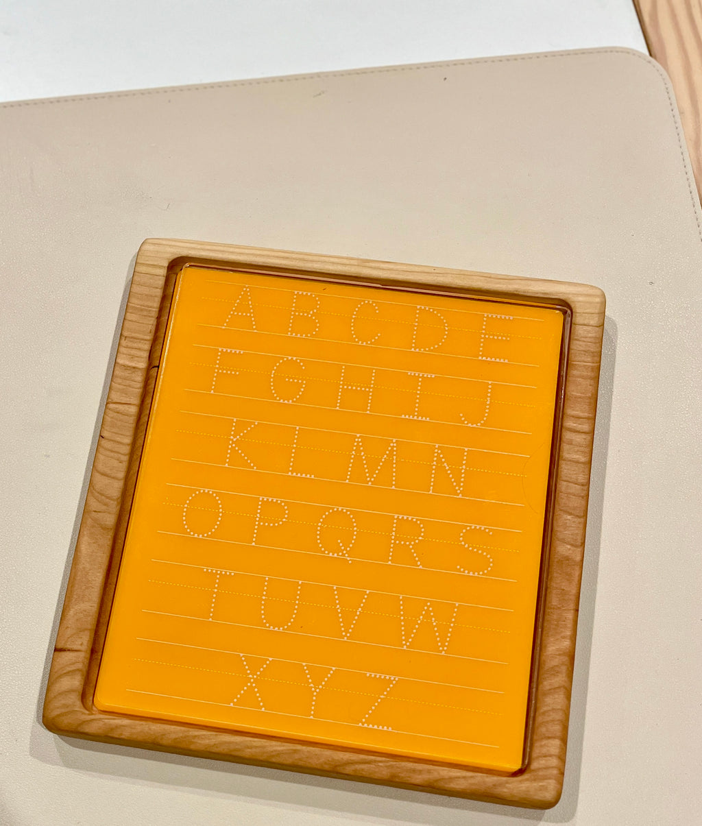 Wooden-framed orange acrylic board with dotted uppercase alphabet letters for handwriting practice on light background