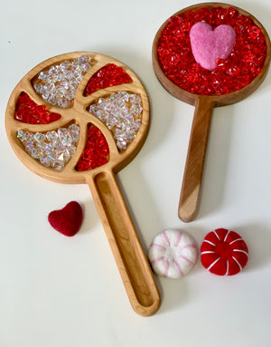 Wooden sensory trays filled with red and clear acrylic gems and pink and red felt heart shapes on white surface