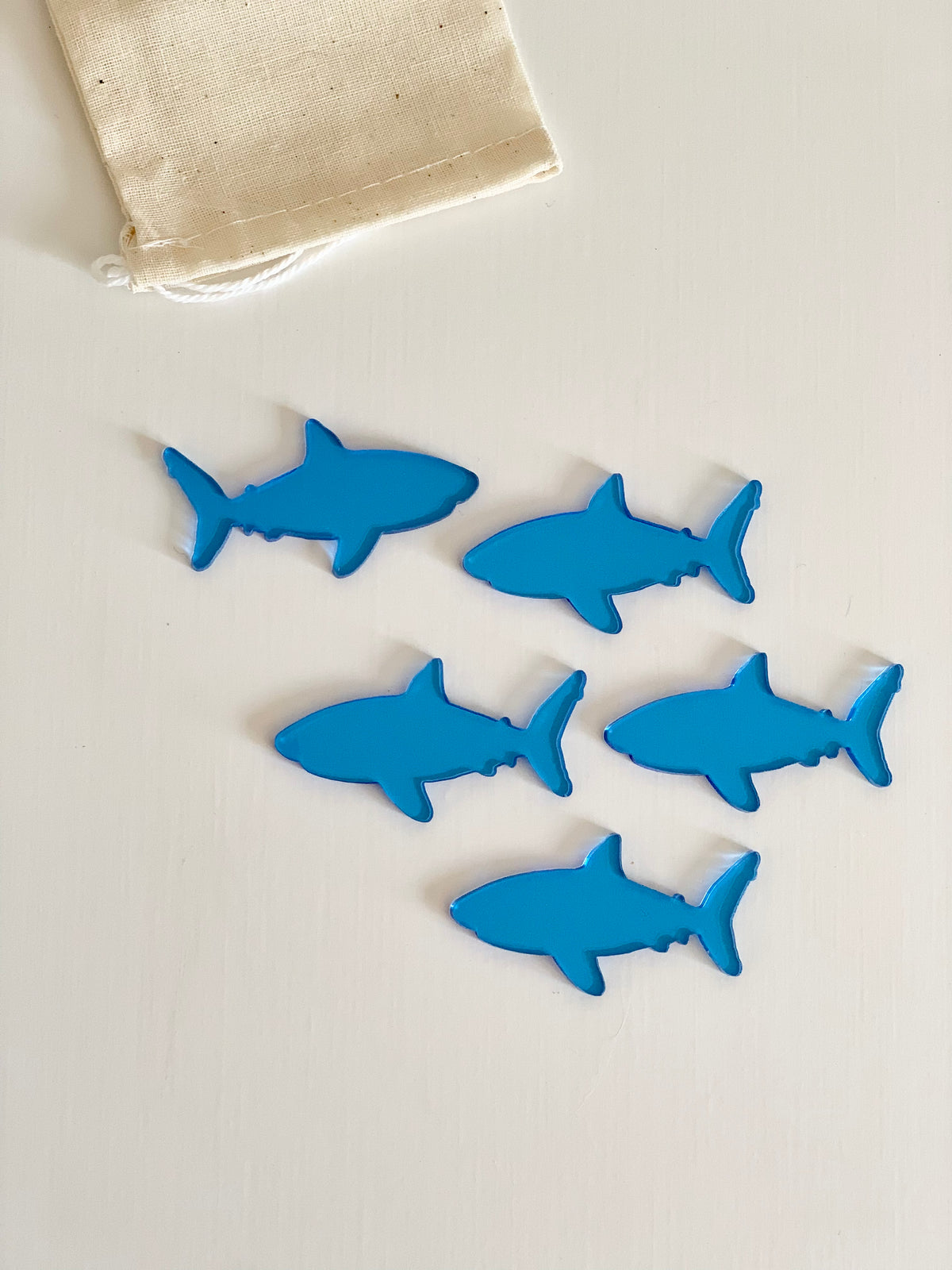 Set of six blue shark-shaped dry erasable pieces with natural drawstring storage bag on white surface