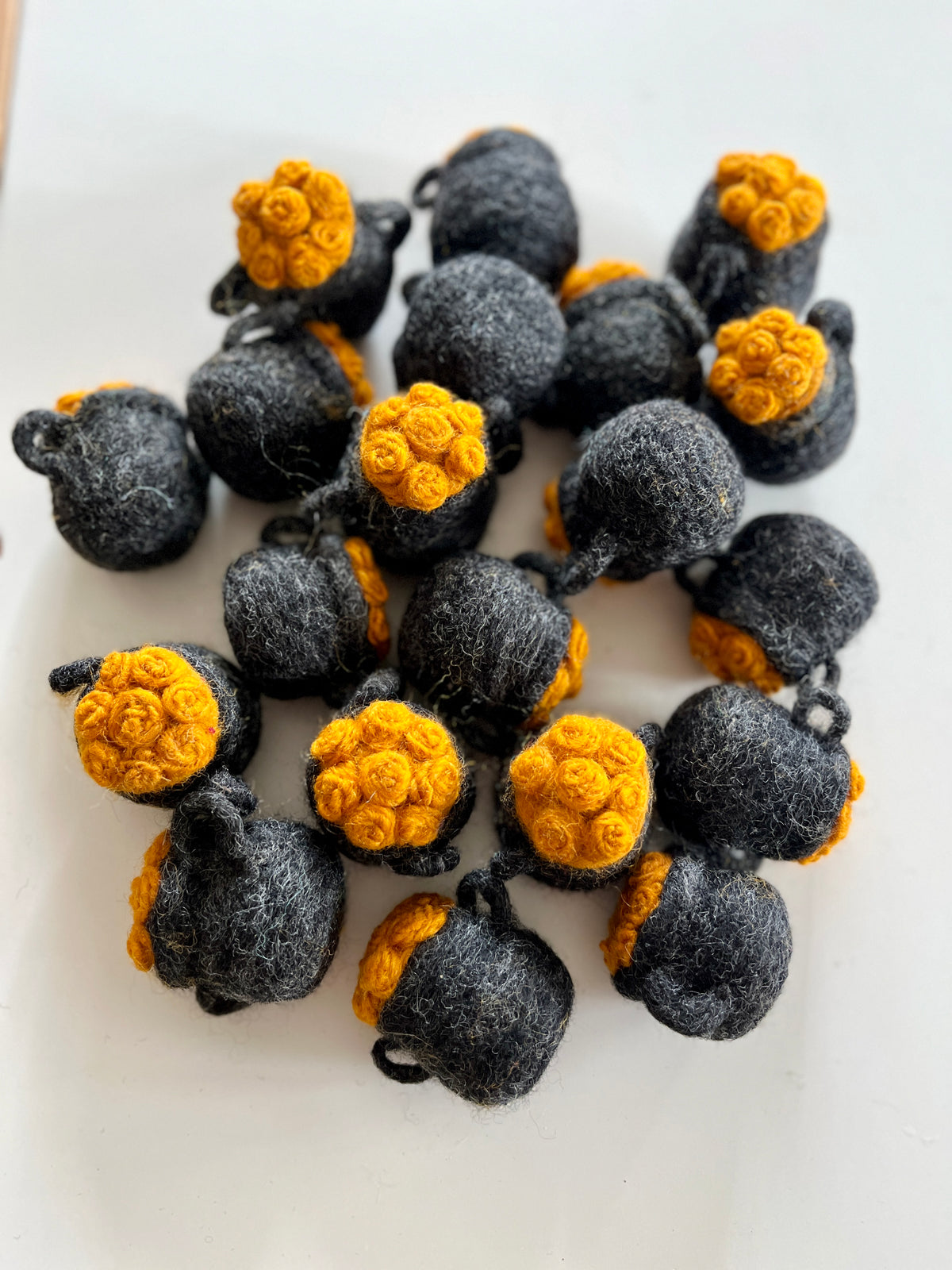 Cluster of small handmade black felt pots with bright orange textured tops scattered on white surface