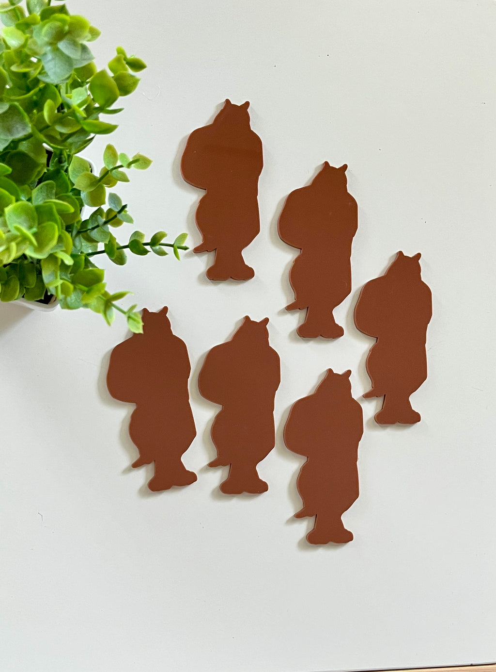 Six brown bear-shaped cutouts arranged near a small green leafy plant on a white surface