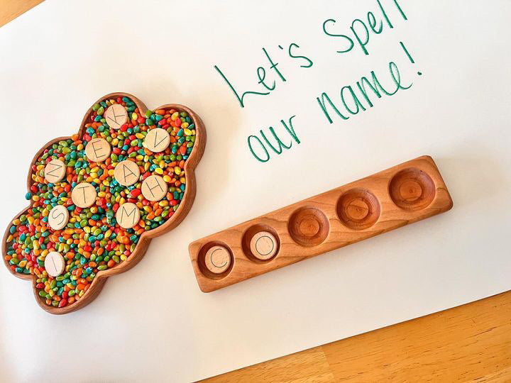 Cloud-shaped wooden sensory tray filled with colorful beads and wooden letter tiles beside a wooden holder on table