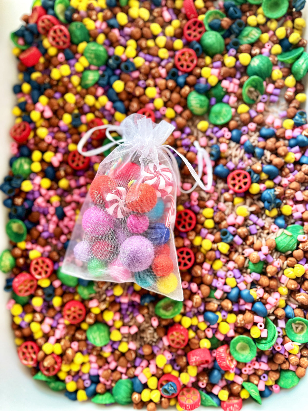 Small organza bag filled with colorful felt balls and candy-shaped beads on a vibrant mix of beads background