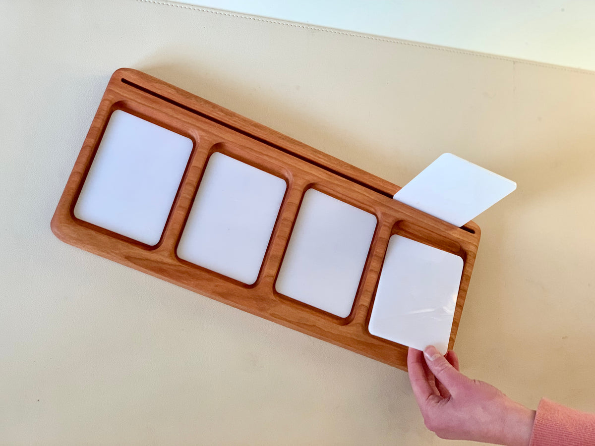 Wooden tray with four rectangular white cards, one card being pulled out by a hand on a light surface