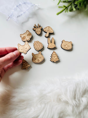 Hand holding wooden animal and nature-themed cutout shapes including fox, bear, rabbit, pinecone, deer, mushroom, and trees on white surface