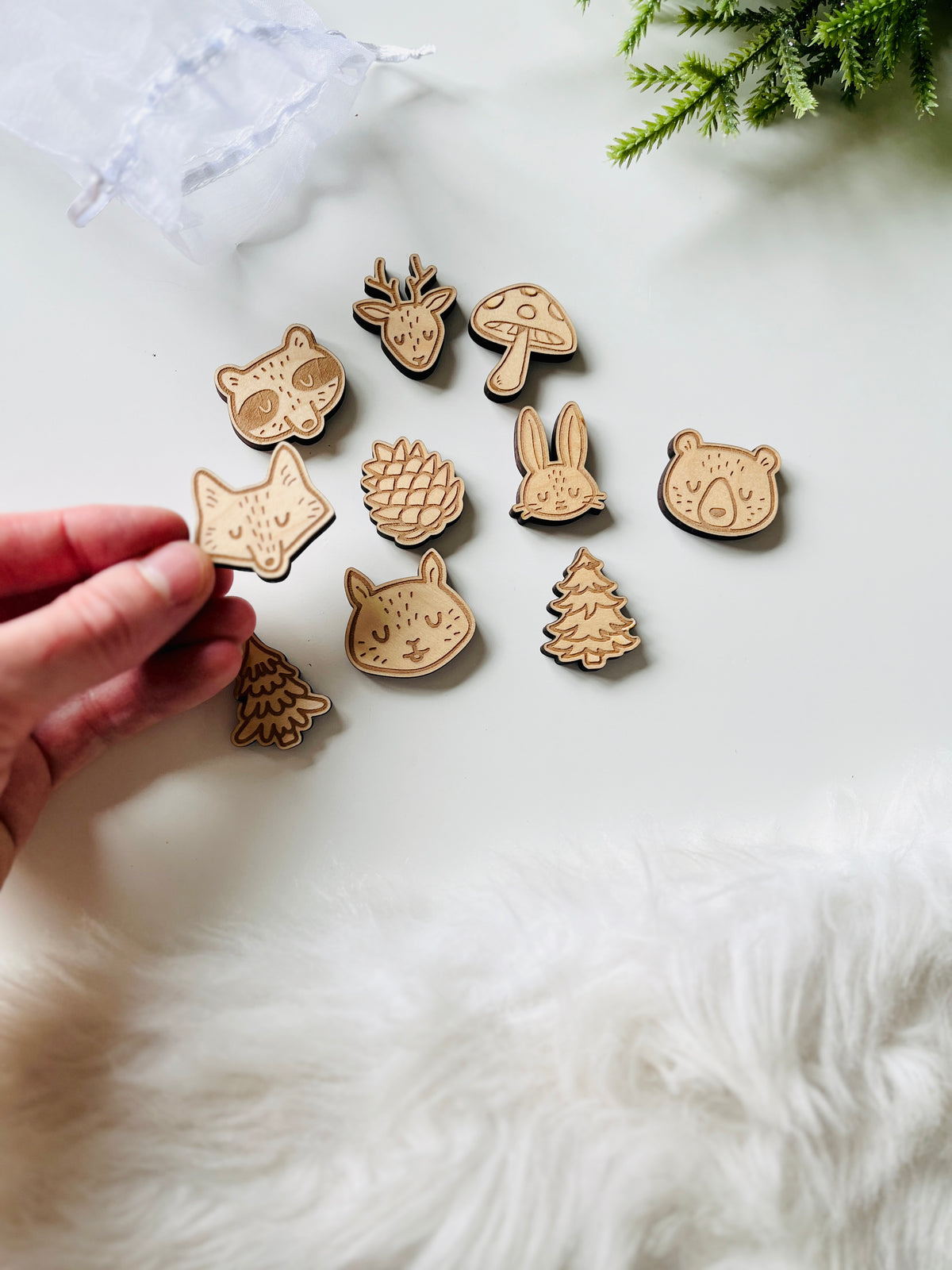 Hand holding wooden animal and nature-themed cutout shapes including fox, bear, rabbit, pinecone, deer, mushroom, and trees on white surface