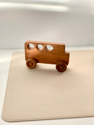 Minimalist wooden toy bus with three circular cut-out windows and round wooden wheels on a light surface