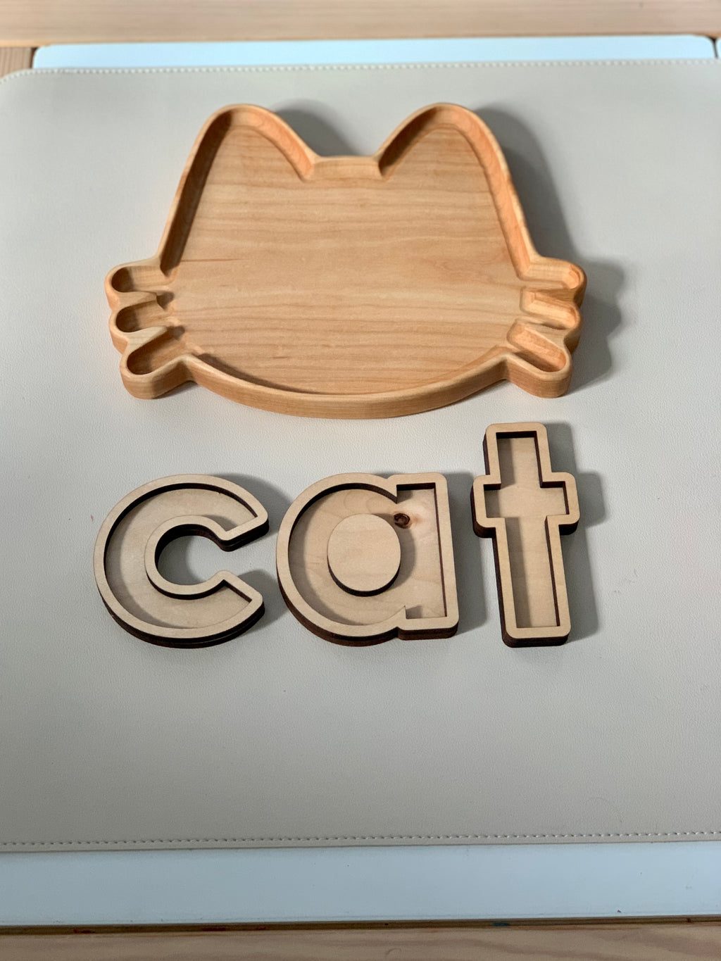 Wooden cat-shaped sensory tray with three wooden letter pieces spelling cat on light surface
