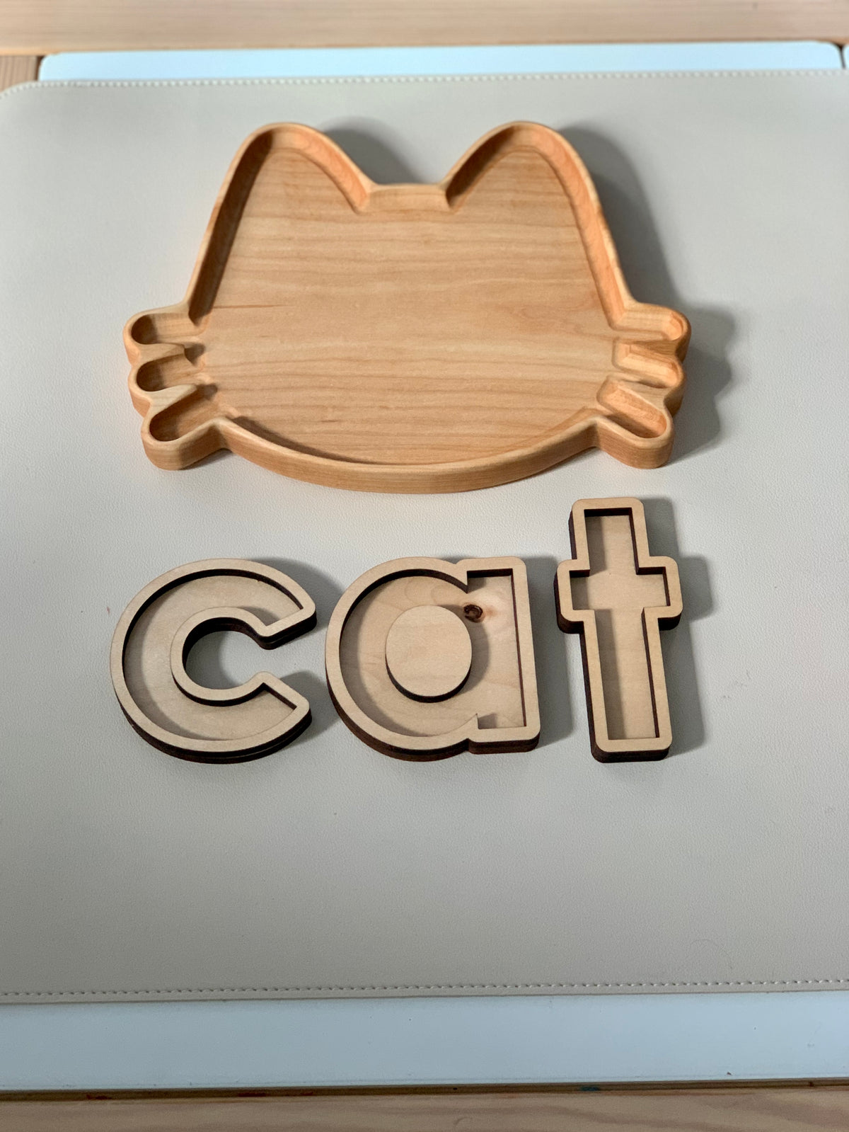 Wooden cat-shaped sensory tray with three wooden letter pieces spelling cat on light surface