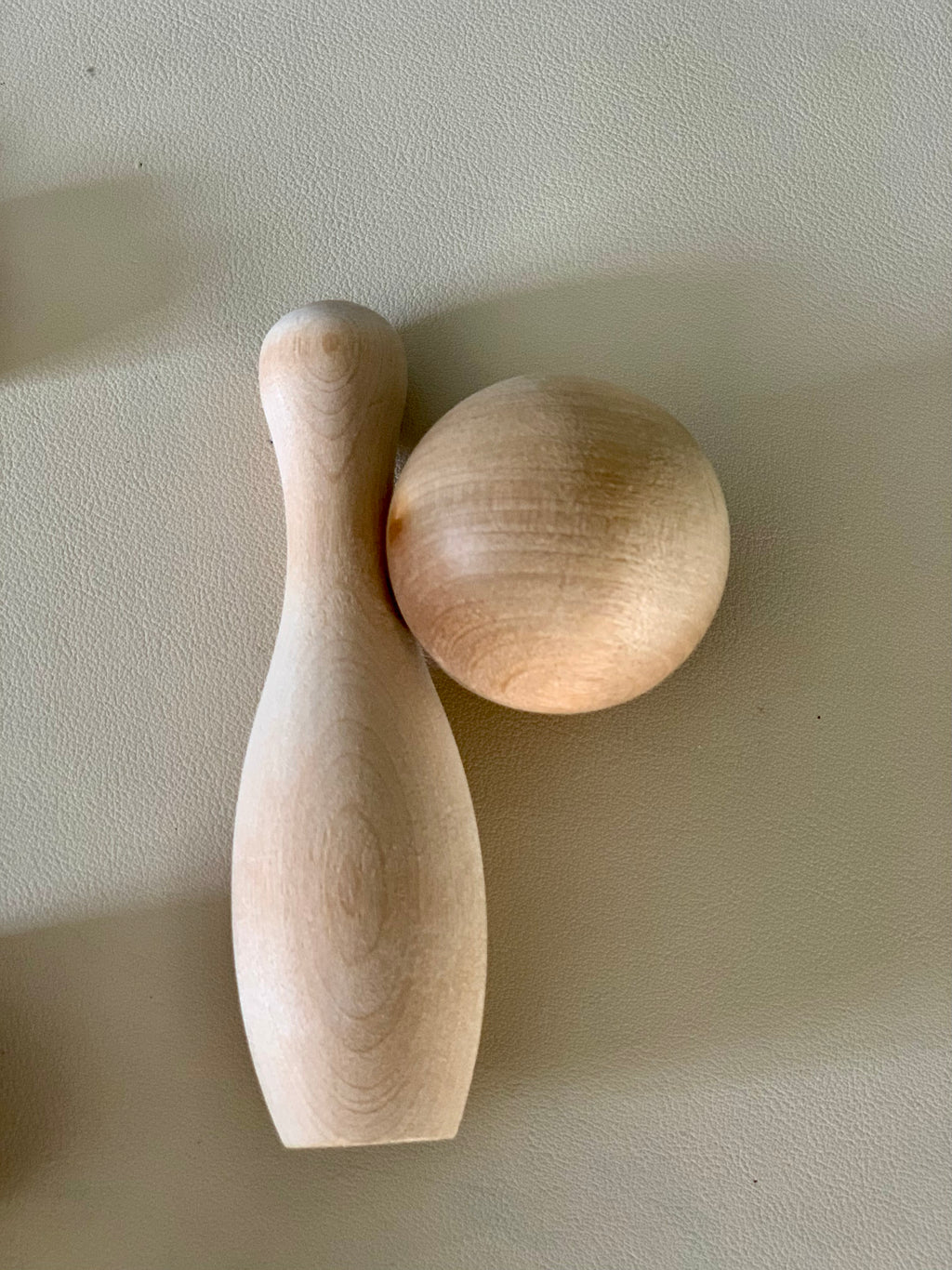 Unfinished smooth natural wood bowling pin and ball resting on a light textured surface