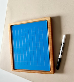 Blue grid drawing board with natural wooden frame and black and white dry erase marker on beige surface