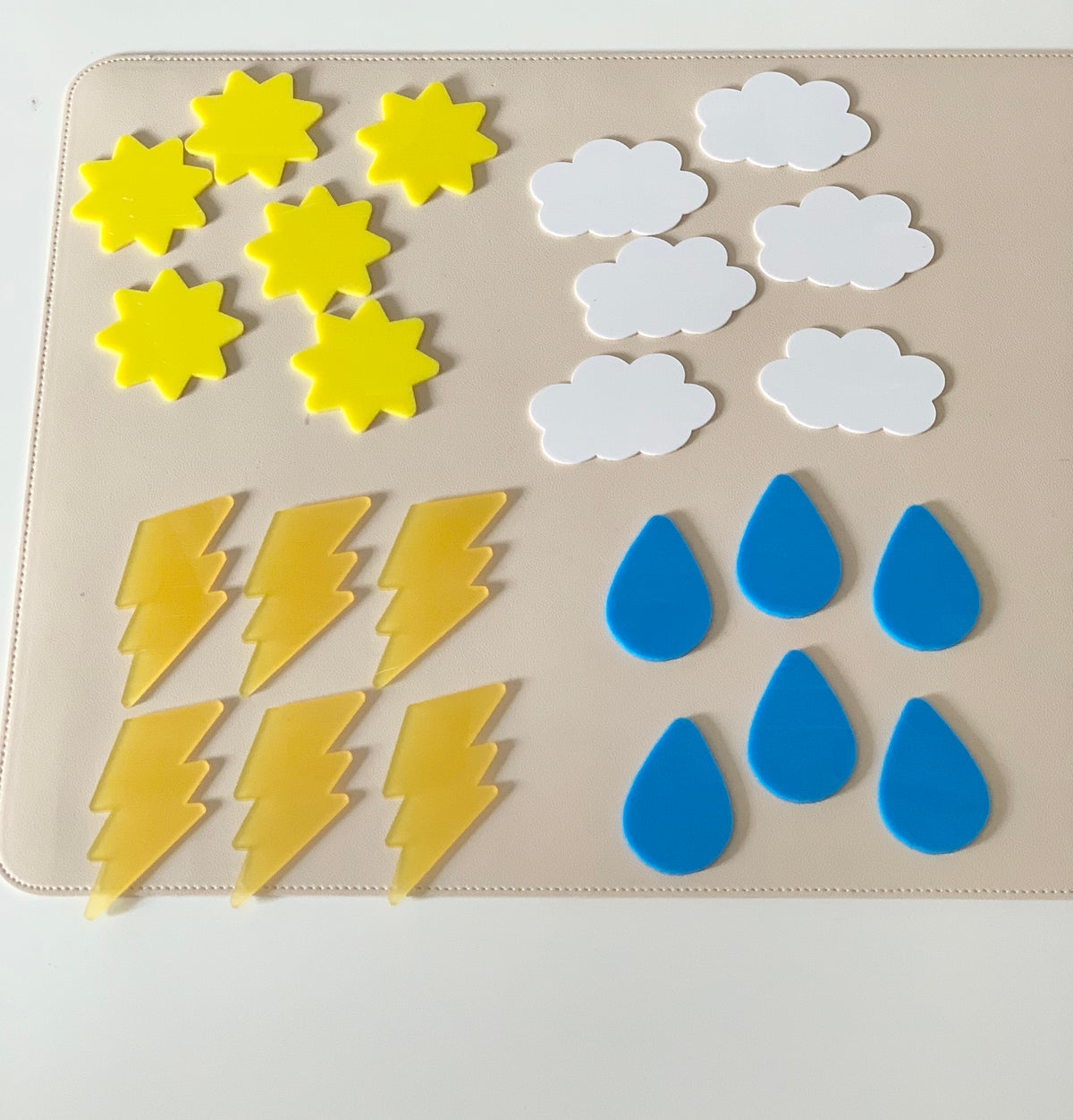 Yellow sun shapes, white cloud shapes, yellow lightning bolts, and blue raindrop shapes arranged on a beige mat