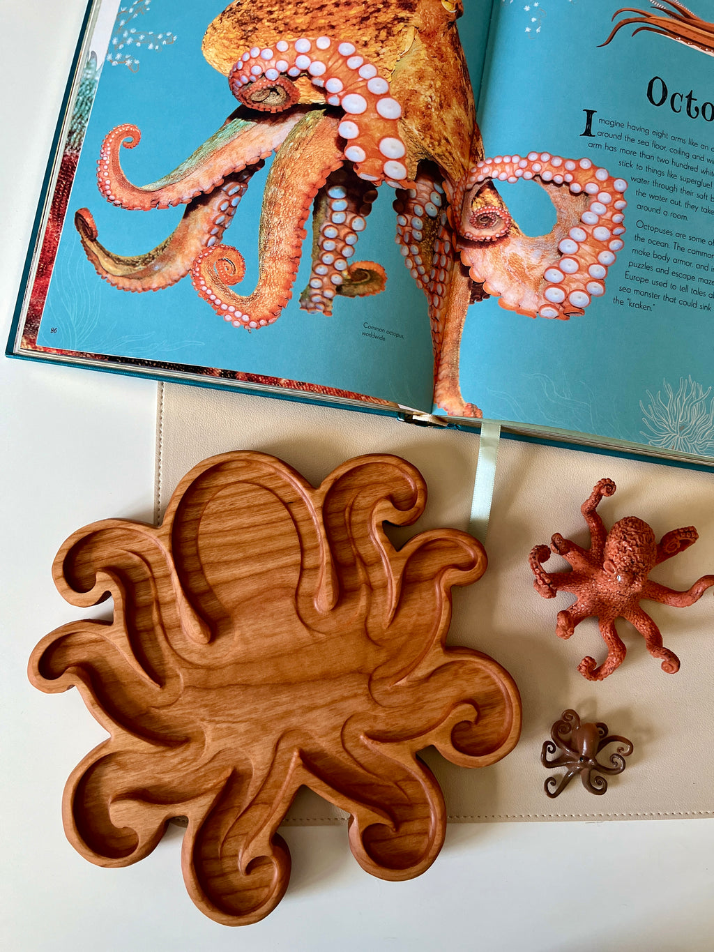 Wooden octopus-shaped tray with multiple curved compartments alongside two octopus figurines on a white surface