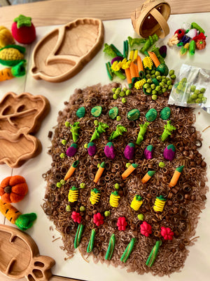 Miniature clay vegetables and pasta arranged artfully on brown rice with wooden trays and felt produce nearby