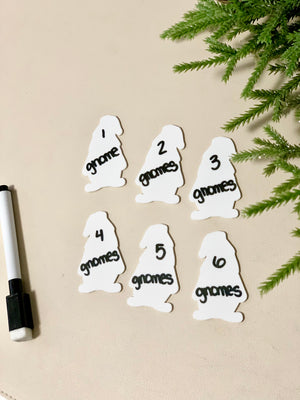 Set of six white gnome-shaped dry erase cards numbered one to six with black marker and green plant on beige surface
