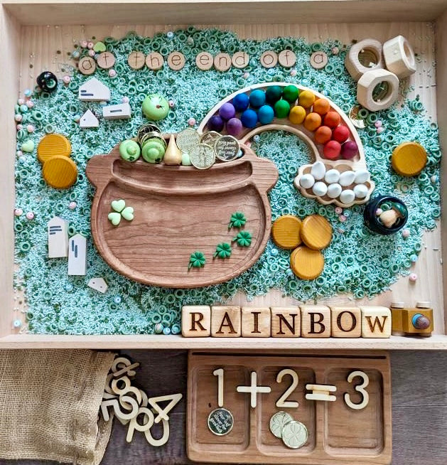 Wood alphabet blocks arranged to spell RAINBOW with wooden tray showing 1+2=3 and rainbow-themed learning toys on blue beads
