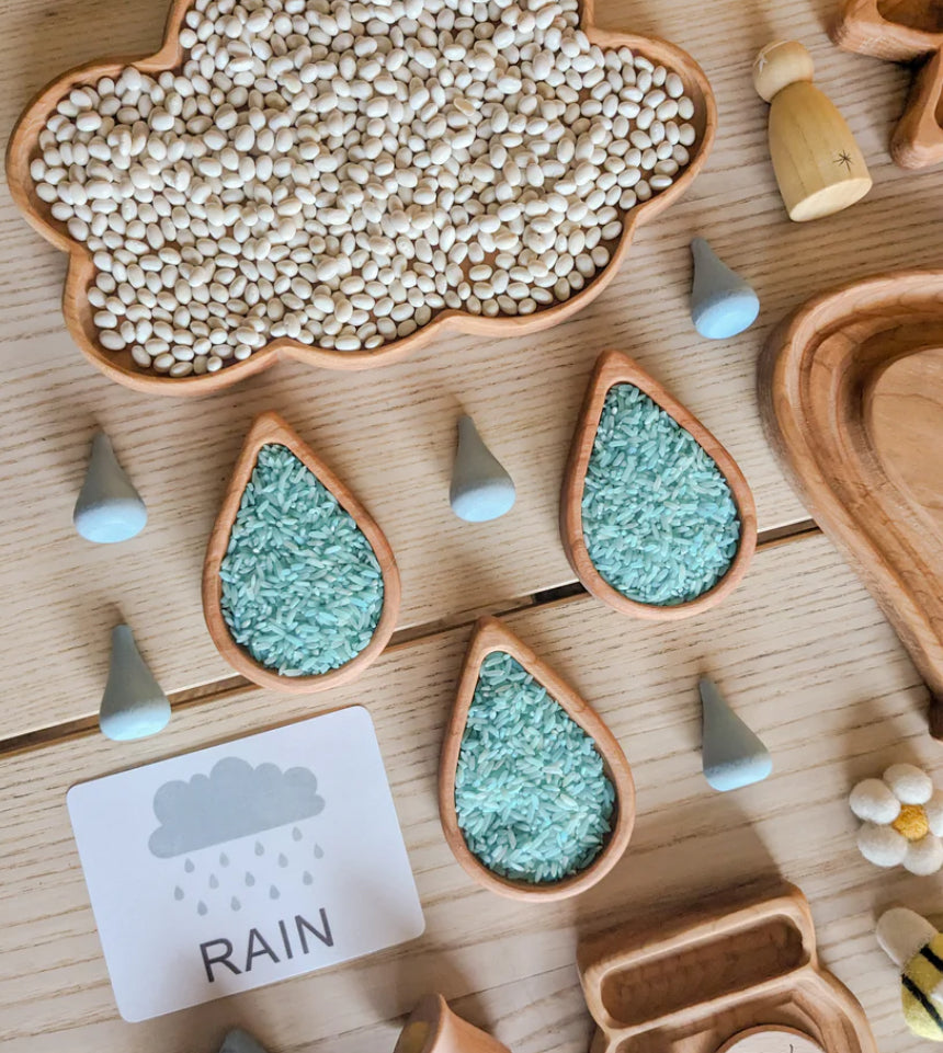 Wooden rain drop plates filled with blue rice and wooden cloud tray filled with white beans on light wood surface