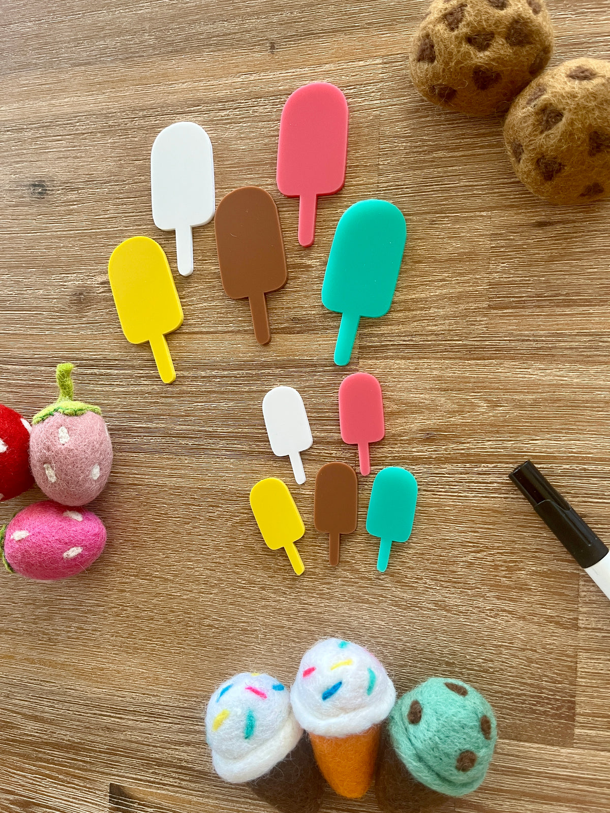 Little Dry Erasables - Popsicles featuring handcrafted wooden popsicle shapes in assorted bright colors arranged on a wood surface with felt food pieces and a black marker, homeschool education resources.