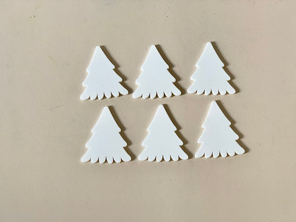 Set of six white pine tree-shaped dry erasable wooden pieces on beige surface with smooth finish