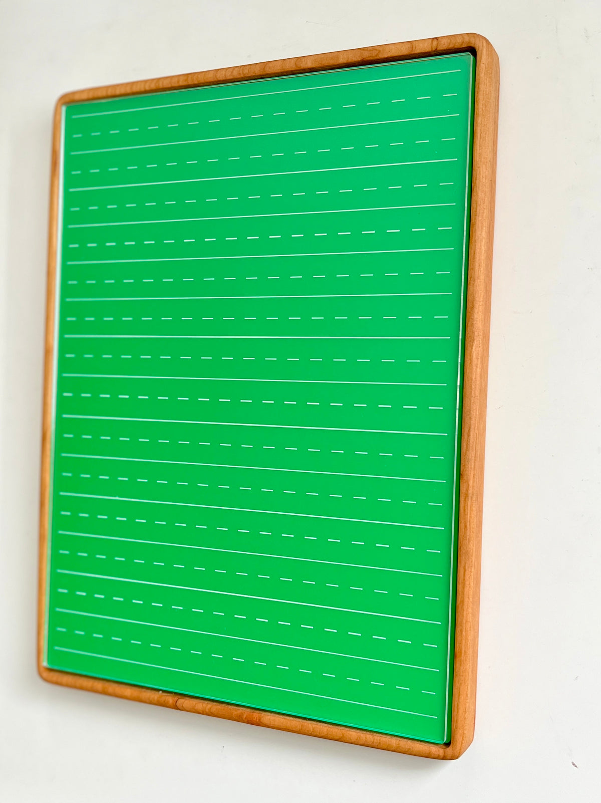 Tall rectangular wooden sensory tray holding green dry erase insert with white dashed handwriting lines on white background