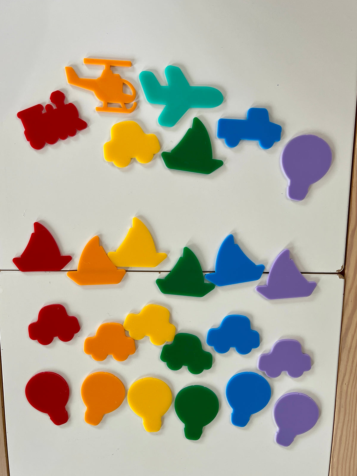 Colorful plastic vehicle and balloon-shaped magnets arranged on a white surface with a wooden edge visible