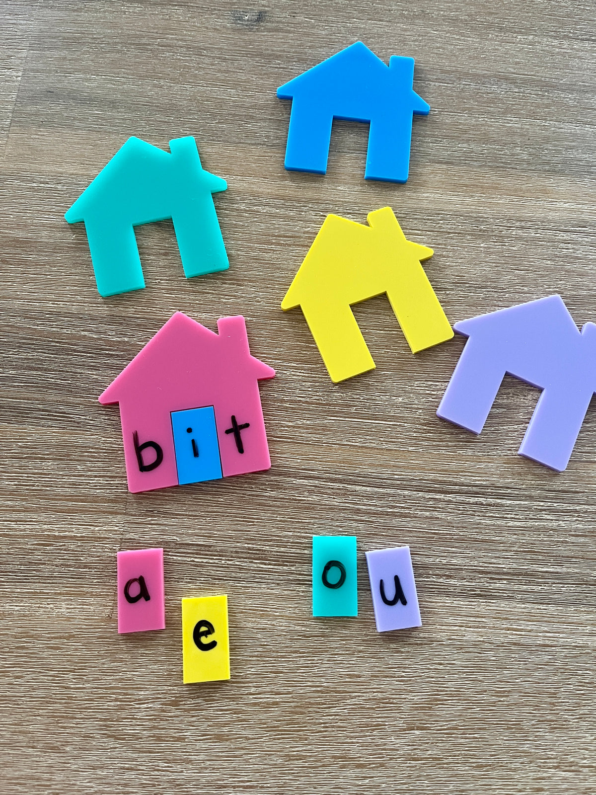 Little Dry Erasables - Houses for CVC, Math + More featuring colorful plastic house shapes with removable vowel tiles spelling "bit" and extra vowel pieces on a wooden surface, handcrafted homeschool education resources.
