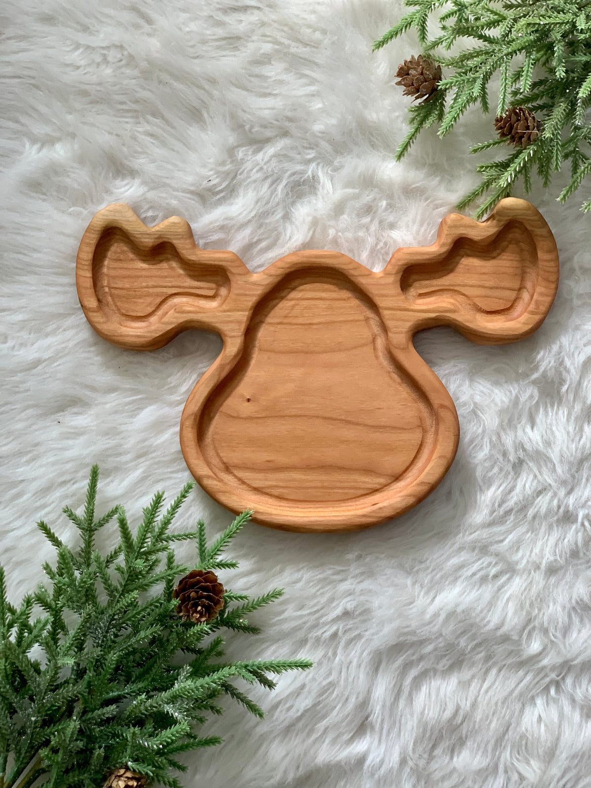 Wooden moose-shaped sensory tray on soft white fur with pine branches and pinecones around edges