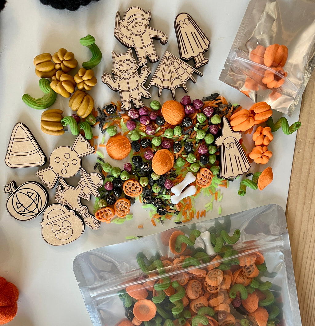 Assorted Halloween-themed wooden cutouts, colorful pasta shapes, and small pumpkin decorations on a white surface