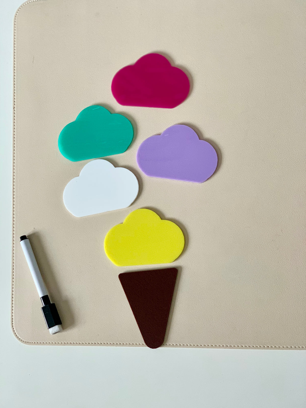 Colorful cloud-shaped pieces and a brown triangle arranged on a beige surface next to a black and white marker
