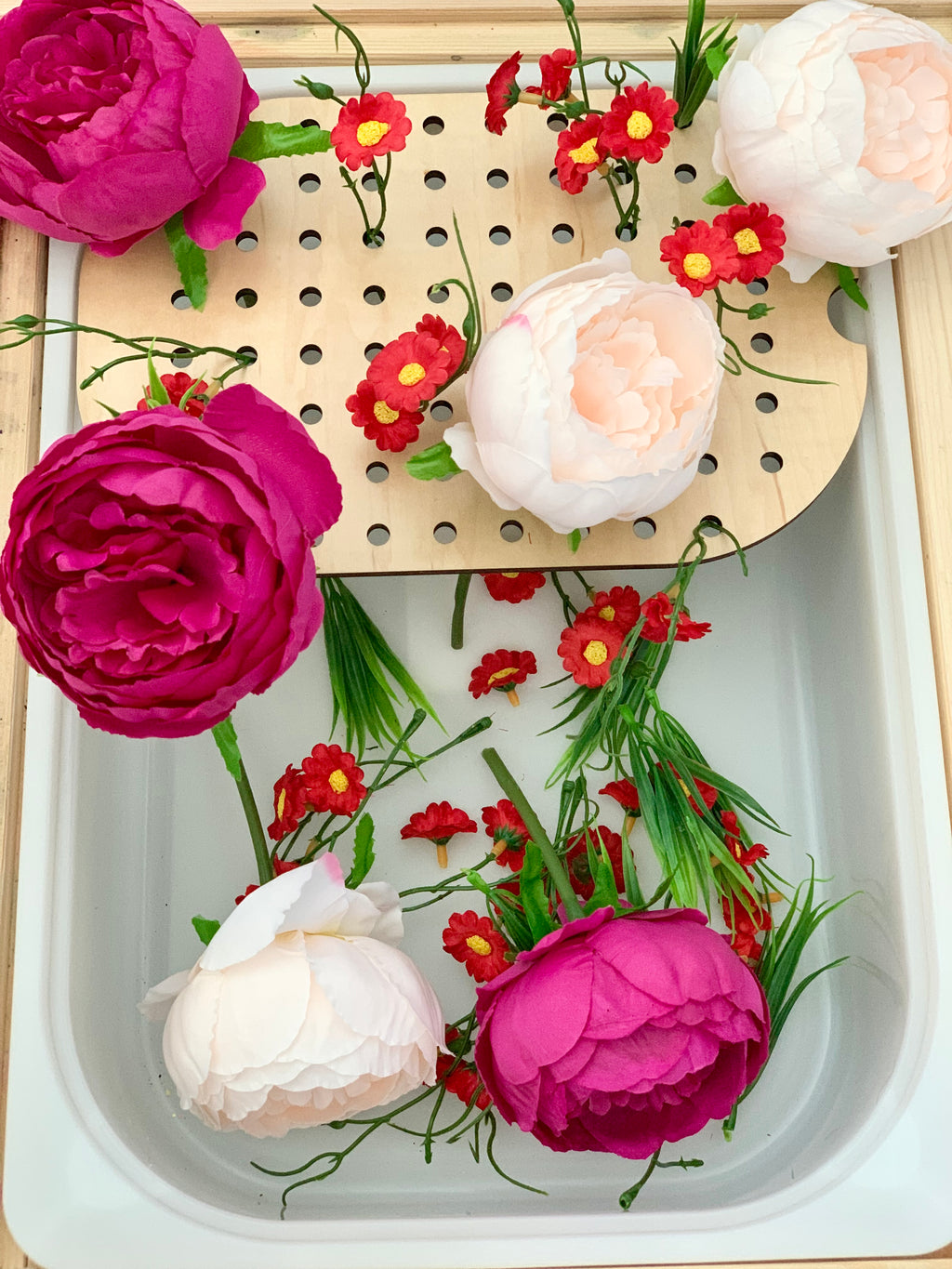 Wooden peg board insert with small holes for golf tees decorated with pink and red artificial flowers inside white bin