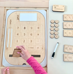 Wooden cash register insert with dry erase total board, wooden credit cards, play money coins and bills on light wood table