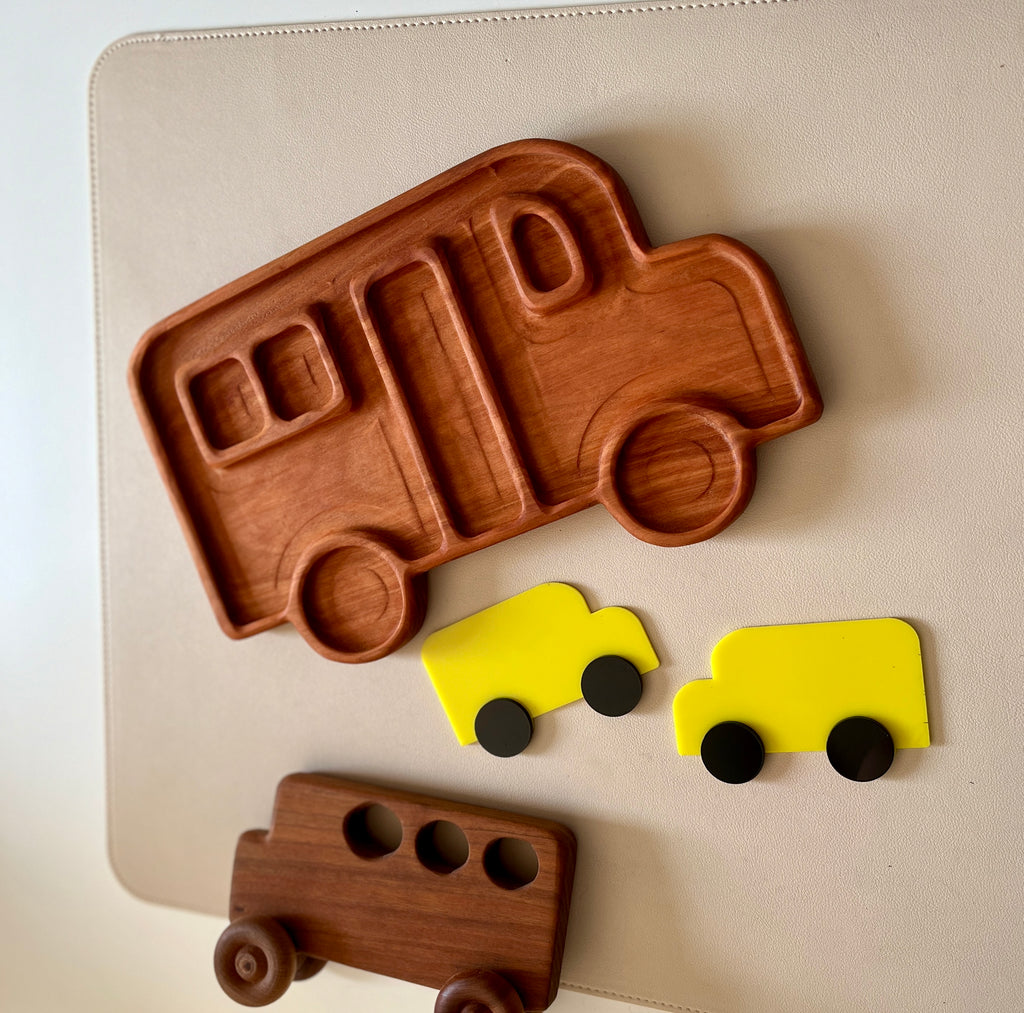 Wooden tray shaped like a camper van with two small yellow toy vans and a dark wooden bus toy on a light surface