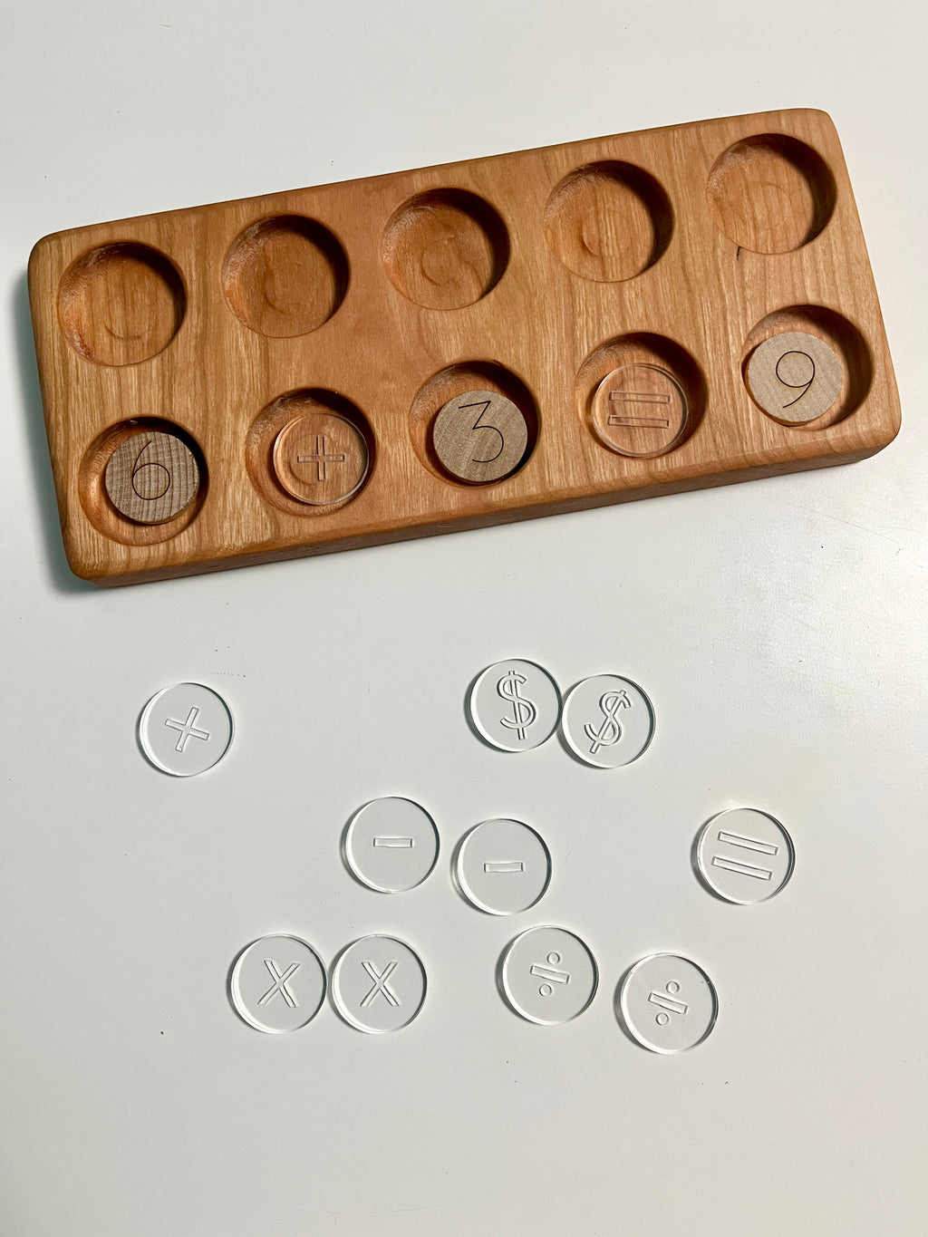 Mini Wood or Clear Acrylic Math Symbol Discs showing a wooden tray with circular slots containing numbers and math symbols, alongside clear acrylic discs featuring engraved arithmetic marks, handcrafted homeschool education resources promoting tactile and sensory learning.