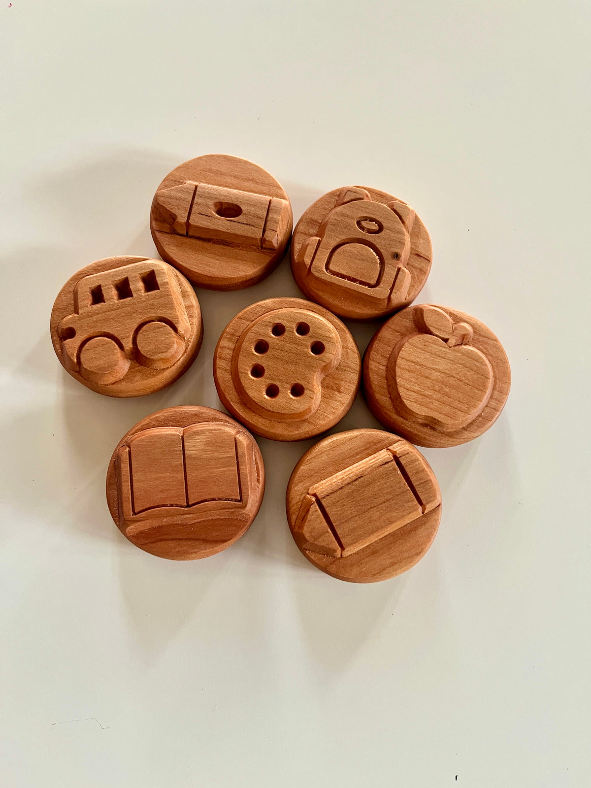 Set of seven round wooden tokens engraved with school-themed icons including backpack, apple, book, bus, and art palette