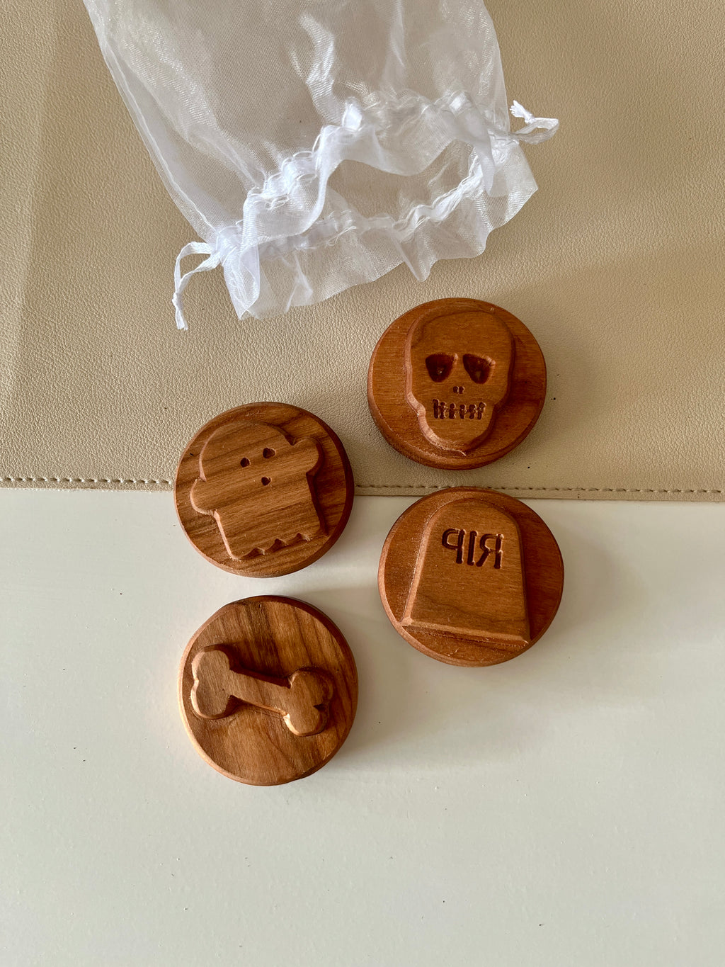 Four round wooden tokens engraved with a zombie, skull, bone, and tombstone next to a white drawstring bag