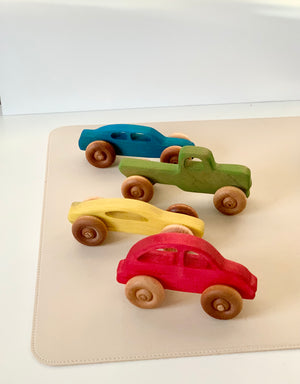 Four wooden toy cars painted in red, yellow, green, and blue with natural wooden wheels on a beige surface