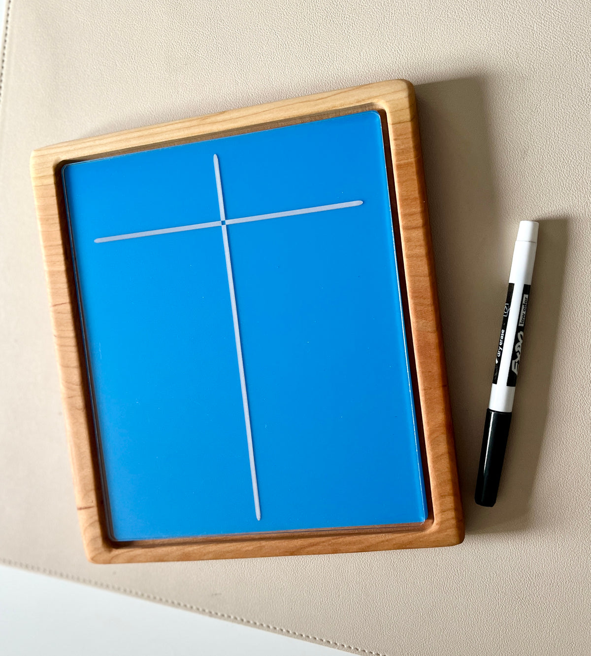Small wooden framed blue drawing board with white cross lines and black dry erase marker on light surface