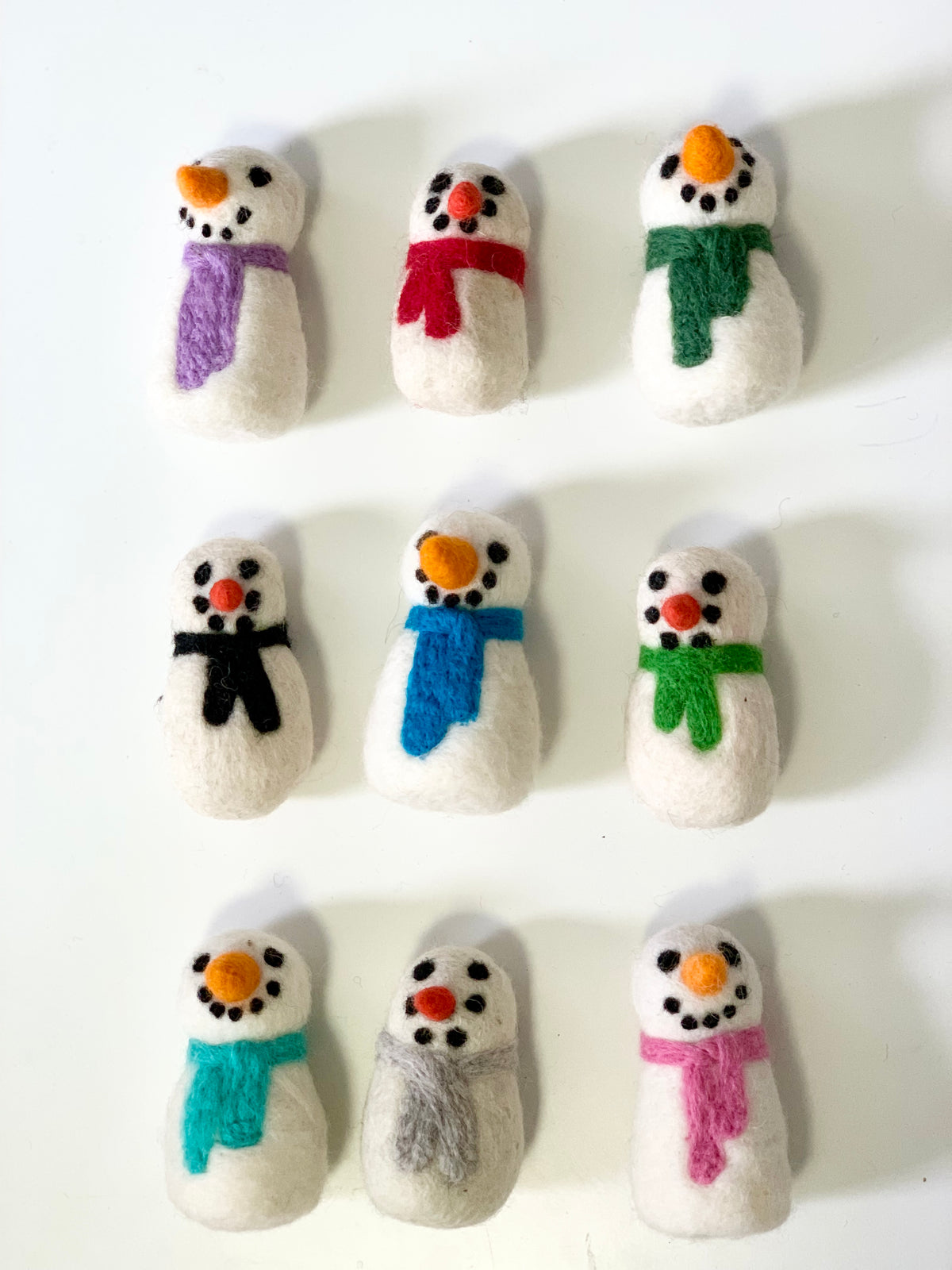 Nine handmade felt snowmen with colorful scarves and carrot noses on white background