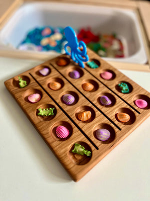 Wooden game board with colorful seashell pieces and green seaweed shapes with a blue octopus figure picker