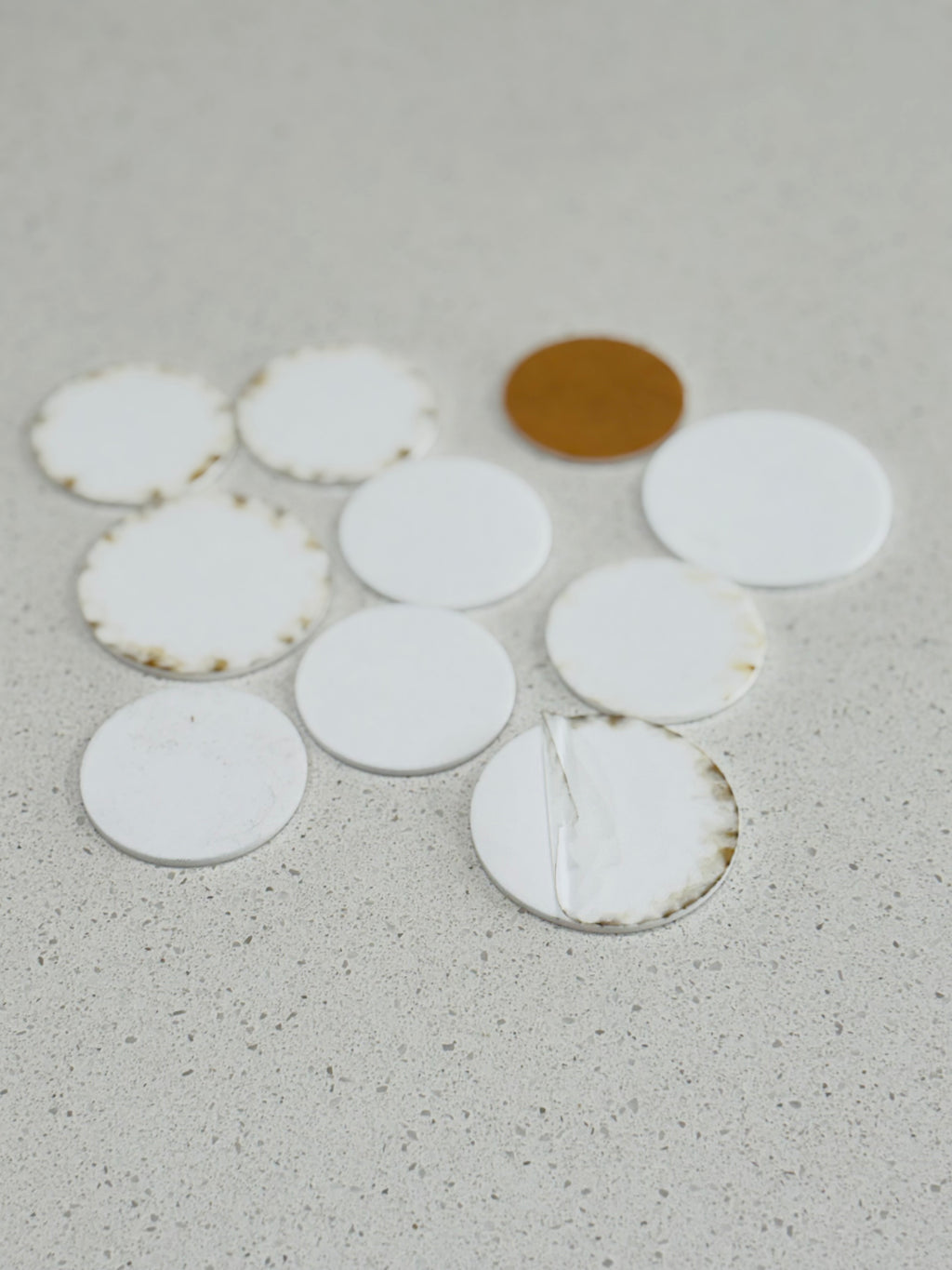 Varied white circular discs with worn edges and one tan disc scattered on a light gray speckled surface