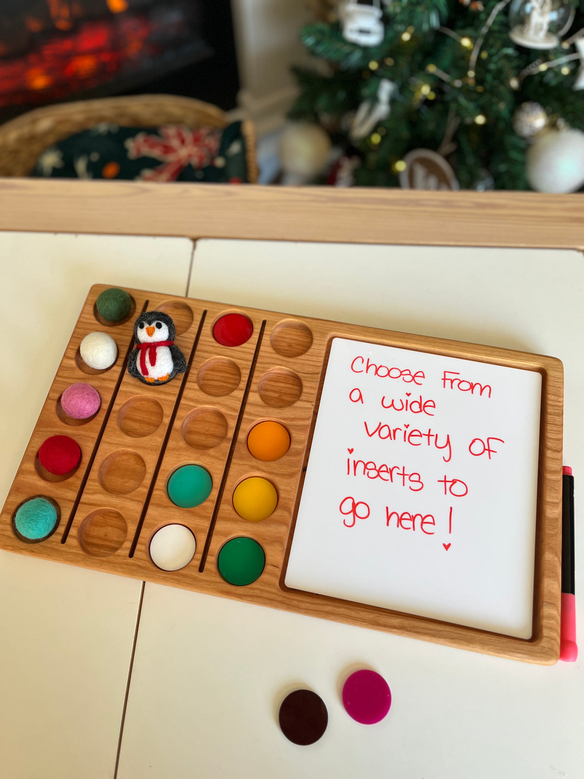 Wooden board with colorful felt balls and a small penguin figure beside whiteboard with red handwriting marker