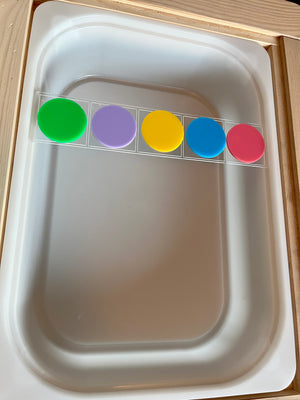 Rectangular clear plastic strip holding five large colorful round discs in green, purple, yellow, blue, and pink colors on a white tray