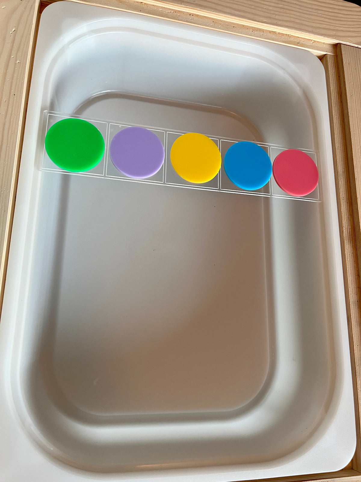 Rectangular clear plastic strip holding five large colorful round discs in green, purple, yellow, blue, and pink colors on a white tray