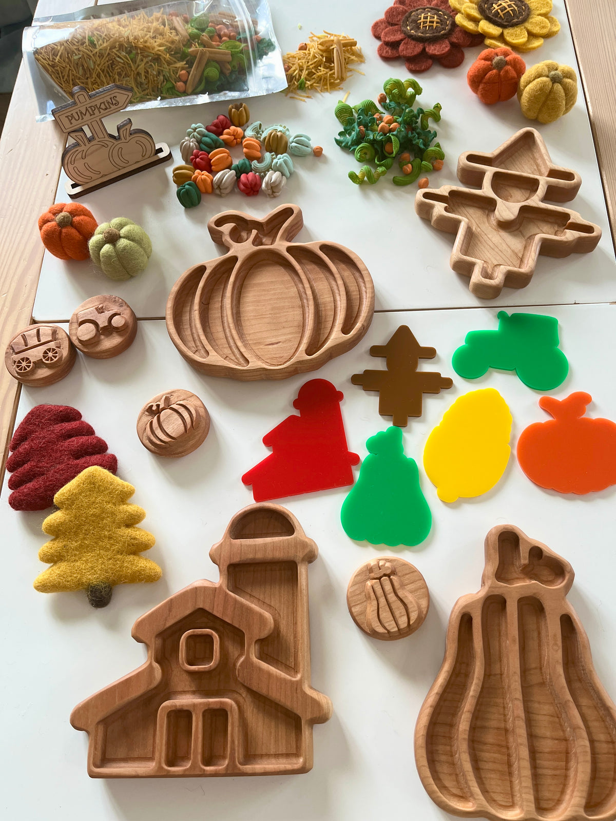 Wooden trays shaped like barn, pumpkin, scarecrow, and fall shapes with colorful felt decorations and mini pumpkins on table