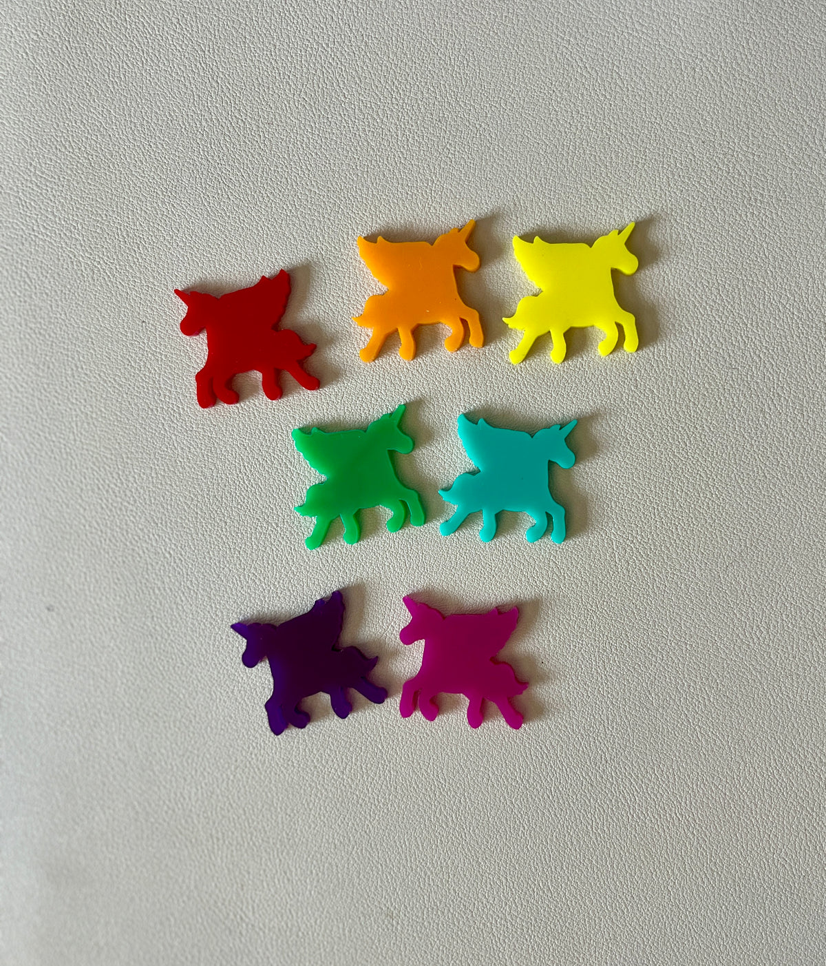 Seven small colorful unicorn-shaped plastic pieces in red, orange, yellow, green, blue, purple, and pink on a light surface